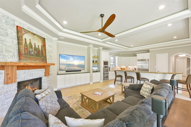 tiled living room featuring ceiling fan, a stone fireplace, crown molding, and a tray ceiling