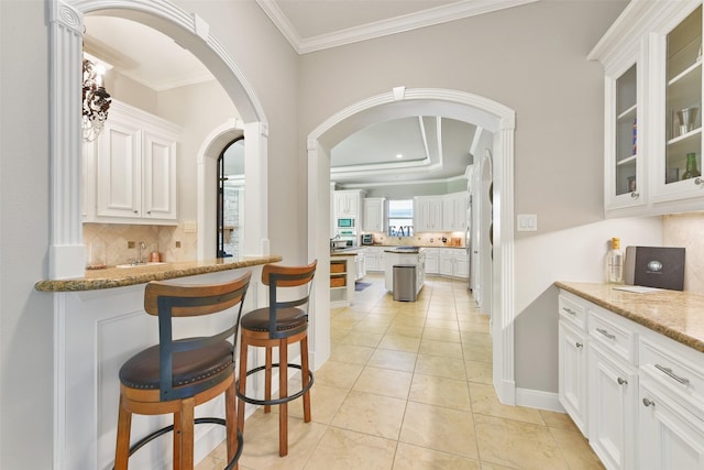 kitchen featuring tasteful backsplash, light stone counters, crown molding, light tile patterned floors, and white cabinets