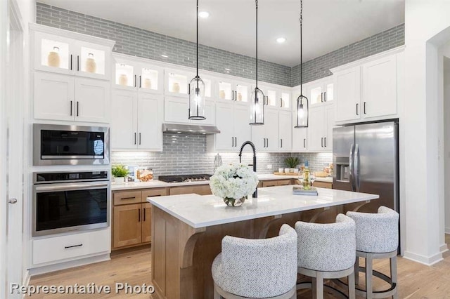 kitchen with pendant lighting, stainless steel appliances, an island with sink, tasteful backsplash, and white cabinets