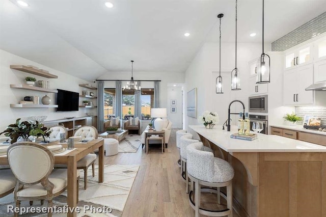 kitchen featuring pendant lighting, light hardwood / wood-style floors, white cabinets, vaulted ceiling, and oven