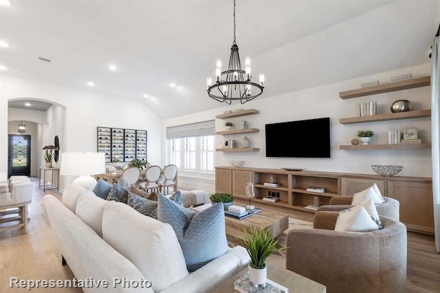 living room featuring an inviting chandelier, vaulted ceiling, and light wood-type flooring