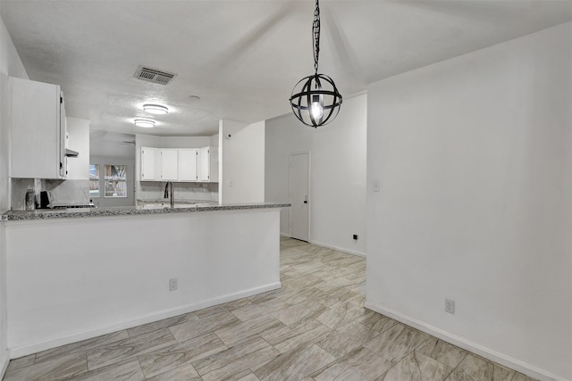 kitchen with white cabinets, pendant lighting, kitchen peninsula, and light stone counters