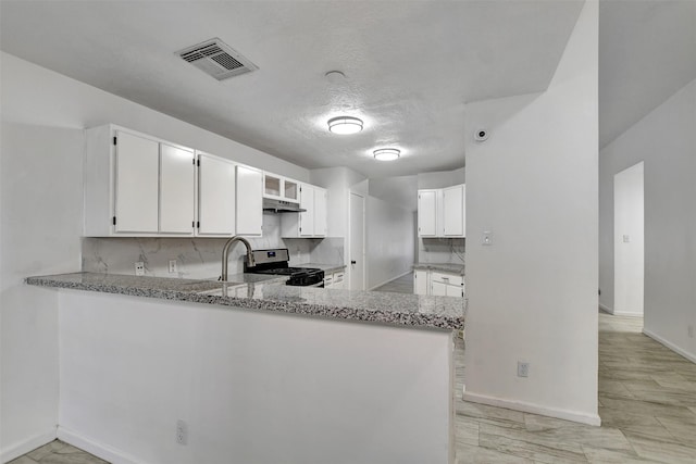 kitchen featuring white cabinets, stainless steel stove, kitchen peninsula, and light stone countertops