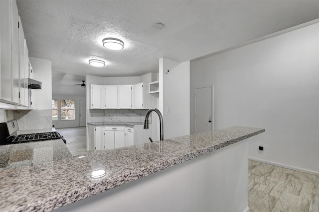 kitchen with kitchen peninsula, light stone countertops, backsplash, range, and white cabinetry