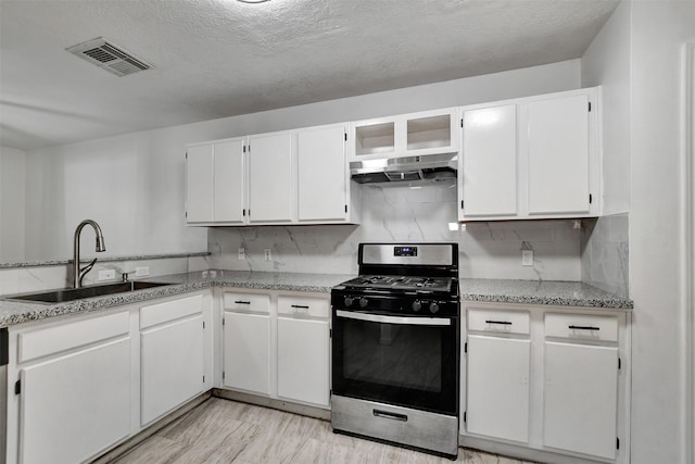 kitchen featuring light stone counters, a textured ceiling, sink, stainless steel gas stove, and white cabinetry