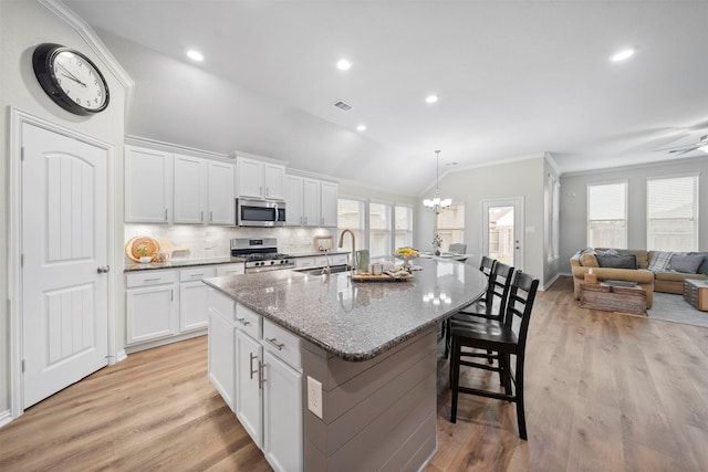 kitchen with white cabinets, a kitchen island with sink, appliances with stainless steel finishes, and vaulted ceiling