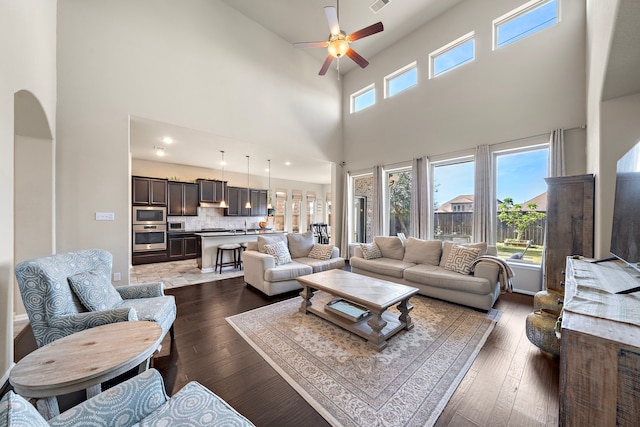 living room with ceiling fan, dark wood-type flooring, and a high ceiling