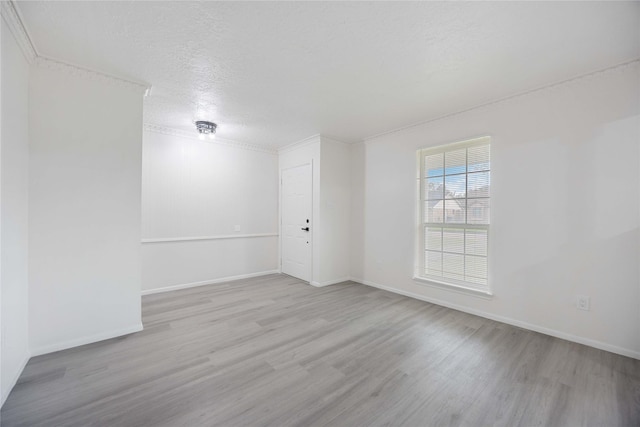 empty room featuring a textured ceiling, light wood-type flooring, and crown molding