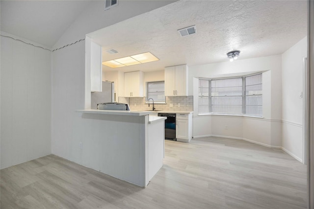 kitchen with kitchen peninsula, white cabinets, light wood-type flooring, and black dishwasher