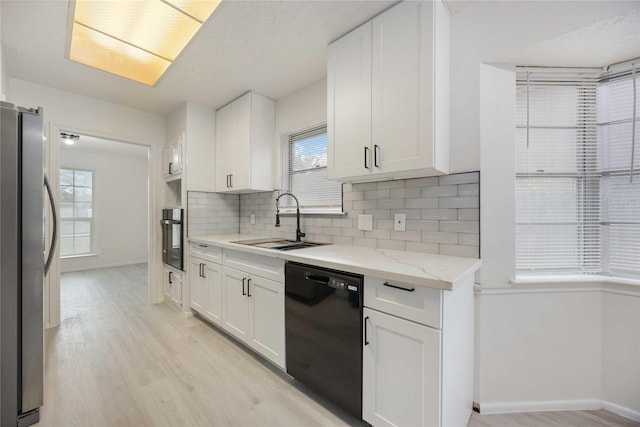 kitchen with black dishwasher, white cabinetry, stainless steel refrigerator, and sink