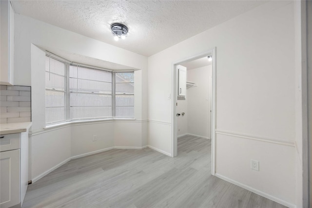 unfurnished dining area featuring a textured ceiling and light wood-type flooring