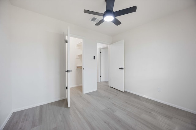 unfurnished bedroom featuring a spacious closet, a closet, ceiling fan, and light wood-type flooring