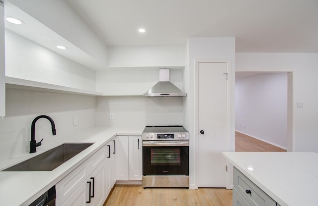 kitchen featuring sink, electric stove, wall chimney range hood, light hardwood / wood-style flooring, and white cabinetry