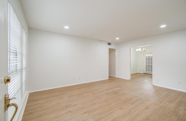 unfurnished room with a notable chandelier, light wood-type flooring, and a wealth of natural light