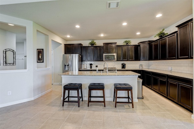 kitchen featuring light stone counters, a center island with sink, and appliances with stainless steel finishes