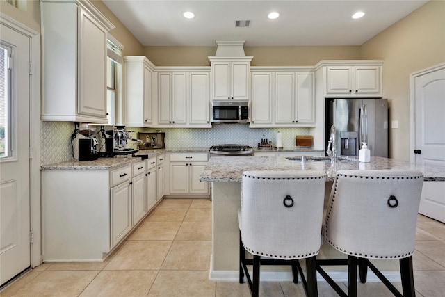 kitchen featuring sink, a center island with sink, light stone counters, and appliances with stainless steel finishes