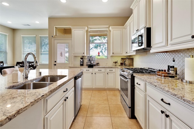 kitchen with light stone countertops, appliances with stainless steel finishes, sink, light tile patterned floors, and white cabinets