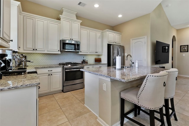 kitchen with light stone countertops, appliances with stainless steel finishes, a center island with sink, white cabinets, and light tile patterned flooring