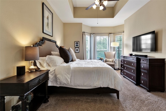 carpeted bedroom with a tray ceiling and ceiling fan