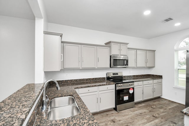 kitchen featuring appliances with stainless steel finishes, light hardwood / wood-style flooring, dark stone counters, and sink