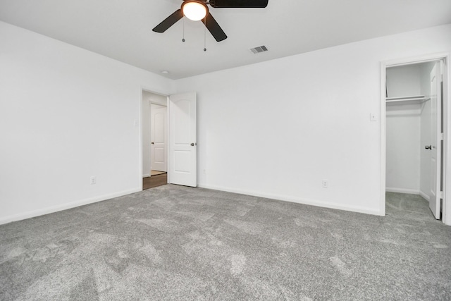 unfurnished bedroom with a closet, a walk in closet, carpet floors, and ceiling fan