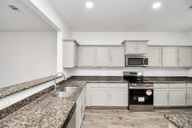 kitchen with dark stone countertops, light hardwood / wood-style floors, sink, and stainless steel appliances