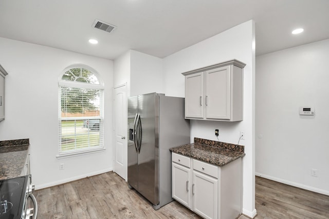 kitchen with stainless steel refrigerator with ice dispenser, stove, light hardwood / wood-style flooring, and dark stone countertops