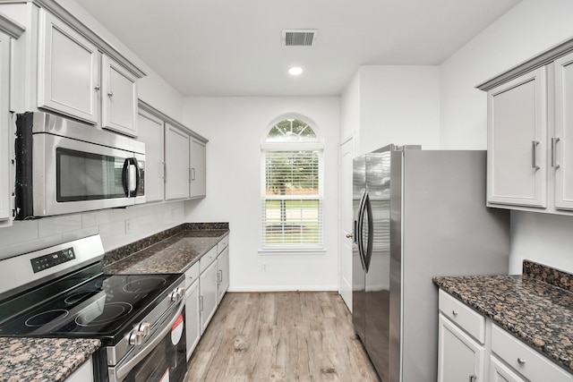 kitchen with gray cabinets, light hardwood / wood-style flooring, dark stone counters, and appliances with stainless steel finishes