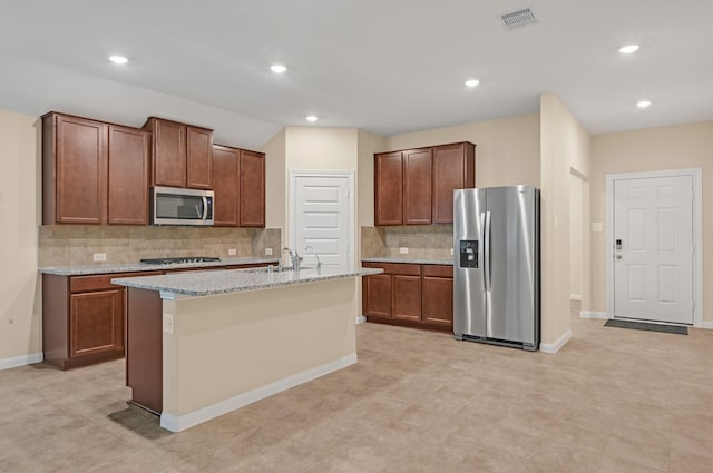 kitchen with sink, light stone counters, backsplash, a kitchen island with sink, and appliances with stainless steel finishes