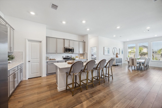 kitchen with decorative backsplash, appliances with stainless steel finishes, a kitchen island with sink, and wood-type flooring