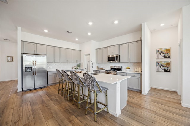 kitchen with a breakfast bar, sink, decorative backsplash, an island with sink, and stainless steel appliances