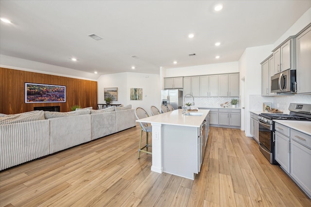 kitchen featuring gray cabinetry, sink, an island with sink, a kitchen bar, and appliances with stainless steel finishes