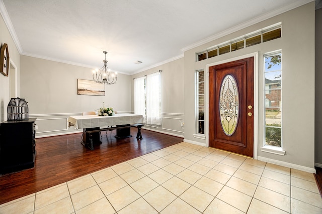 entryway with light tile patterned floors, ornamental molding, and a chandelier