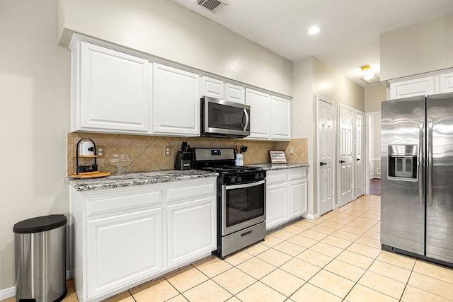 kitchen with light tile patterned flooring, white cabinets, backsplash, stainless steel appliances, and light stone countertops