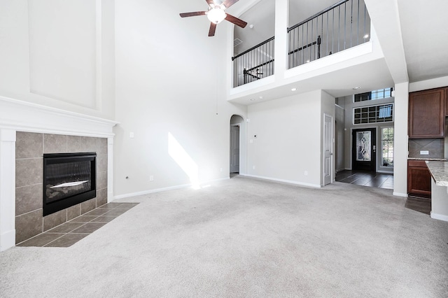 unfurnished living room featuring ceiling fan, a fireplace, a towering ceiling, and light colored carpet