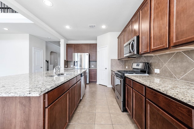 kitchen featuring tasteful backsplash, light stone countertops, stainless steel appliances, and an island with sink