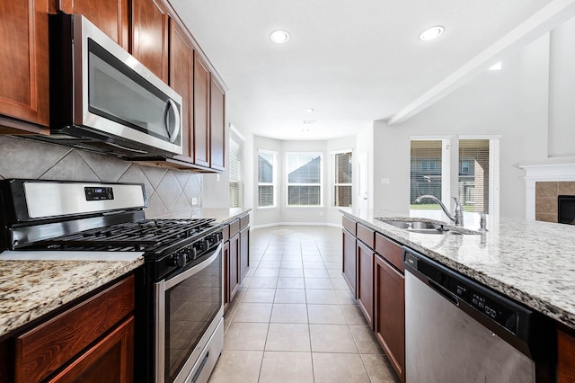 kitchen with sink, stainless steel appliances, light stone counters, a tiled fireplace, and light tile patterned floors