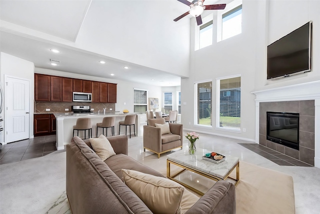 living room featuring ceiling fan, sink, a high ceiling, and a tile fireplace