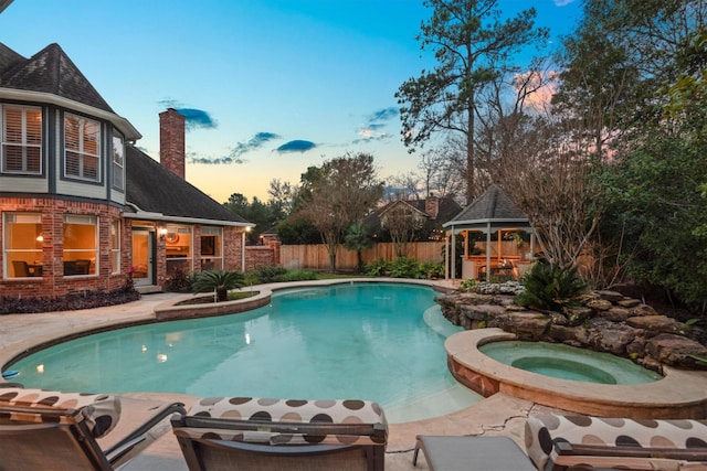 pool at dusk featuring a gazebo and an in ground hot tub