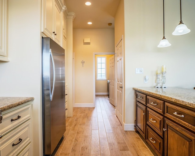 kitchen featuring light stone counters, pendant lighting, stainless steel fridge, and light hardwood / wood-style flooring