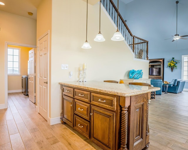 kitchen with decorative light fixtures, ceiling fan, light stone counters, and light hardwood / wood-style floors