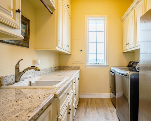 washroom with electric panel, washing machine and dryer, sink, light hardwood / wood-style flooring, and cabinets