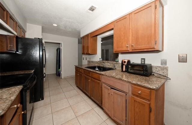 kitchen featuring light stone counters, wall chimney range hood, sink, light tile patterned floors, and black electric range