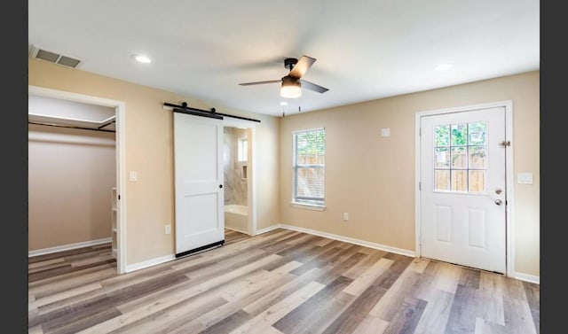 unfurnished bedroom featuring ceiling fan, a barn door, light hardwood / wood-style flooring, ensuite bathroom, and a closet