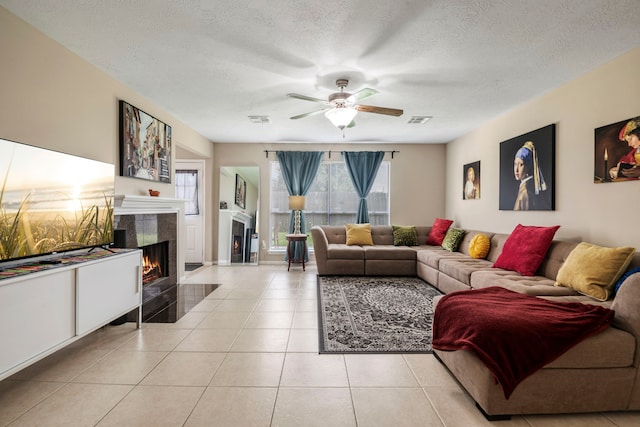 tiled living room with a tile fireplace, ceiling fan, and a textured ceiling