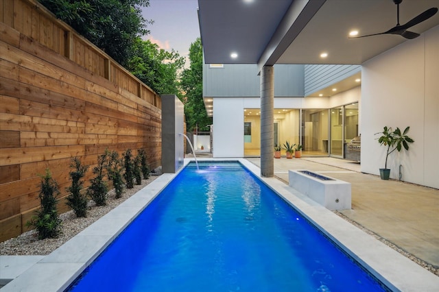 pool at dusk with pool water feature, ceiling fan, and a patio area