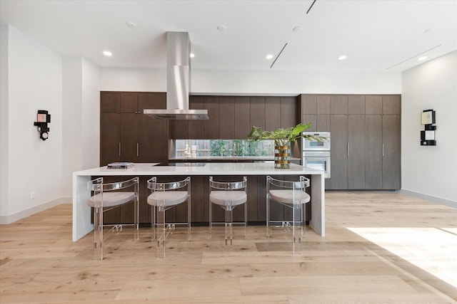 kitchen with dark brown cabinetry, a spacious island, light hardwood / wood-style floors, a breakfast bar area, and range hood