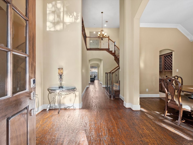 foyer with a towering ceiling, dark hardwood / wood-style flooring, an inviting chandelier, and crown molding