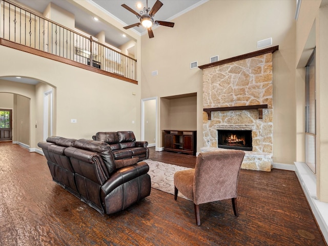 living room with a high ceiling, ceiling fan, a stone fireplace, and dark hardwood / wood-style floors