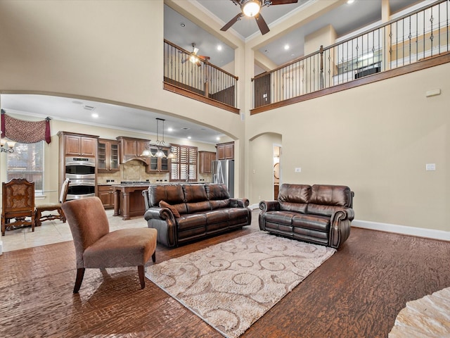 living room featuring ornamental molding, light hardwood / wood-style floors, ceiling fan with notable chandelier, and a high ceiling